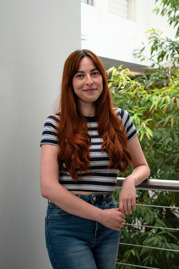 Image of Rebecca - she has long curled orange hair and is wearing a striped top