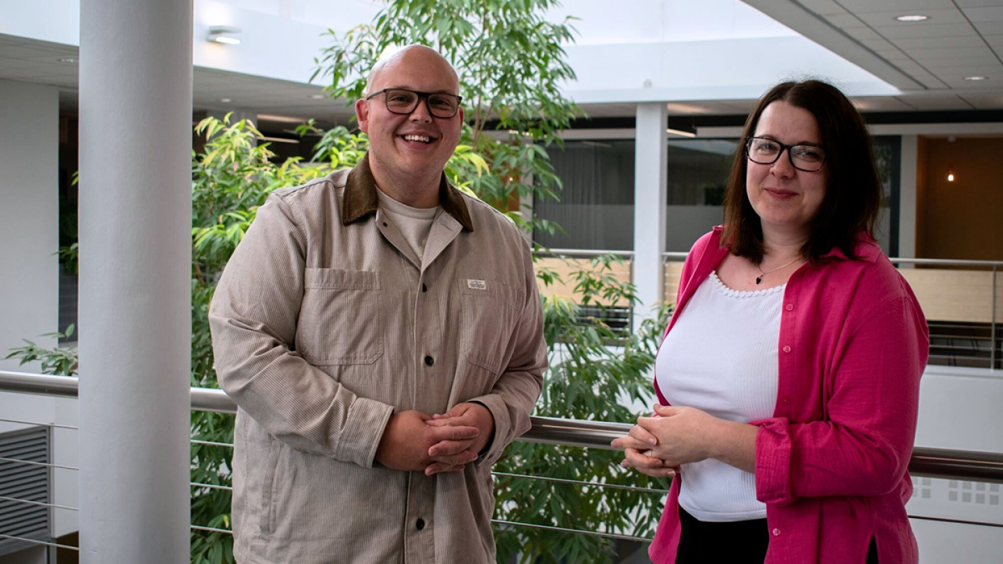Rob Gibson and Leah Charlton pose for the camera smiling. Leah is wearing a white top and pink cardigan while Rob is wearing a sandy coloured jacket.