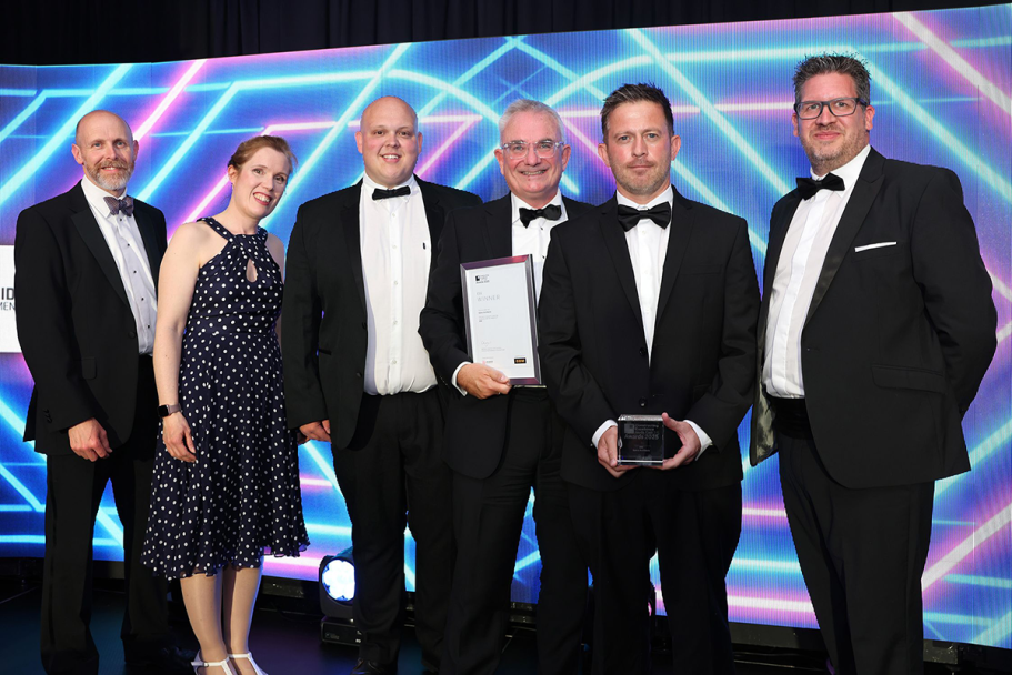 Five men and one woman pose for an photo with an award, they are all in black tie attire.