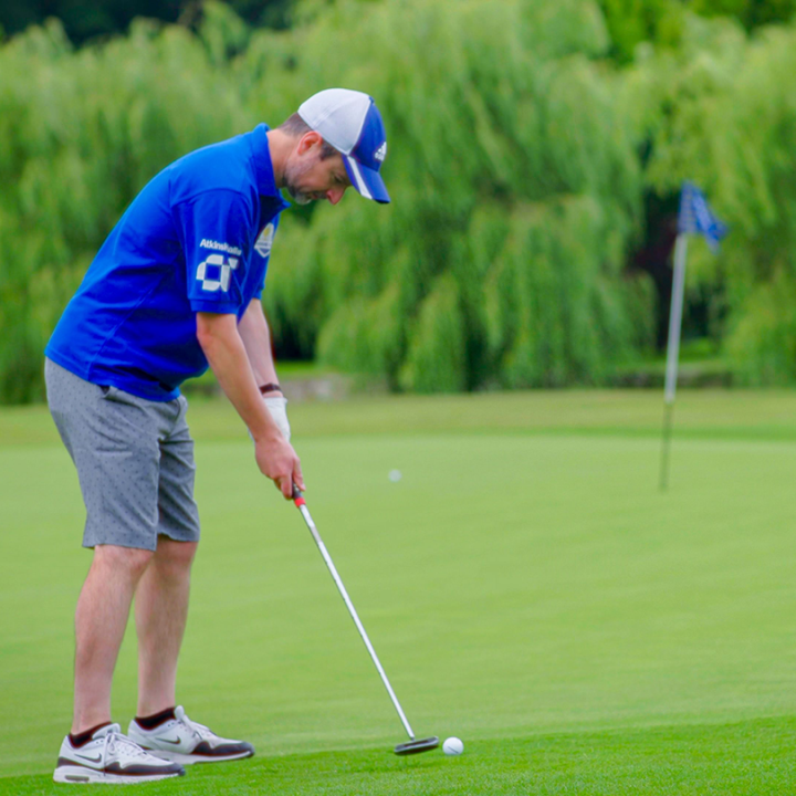 A man with grey shorts, a blue shirt, and a blue and white cap prepares to take a shot while playing golf.