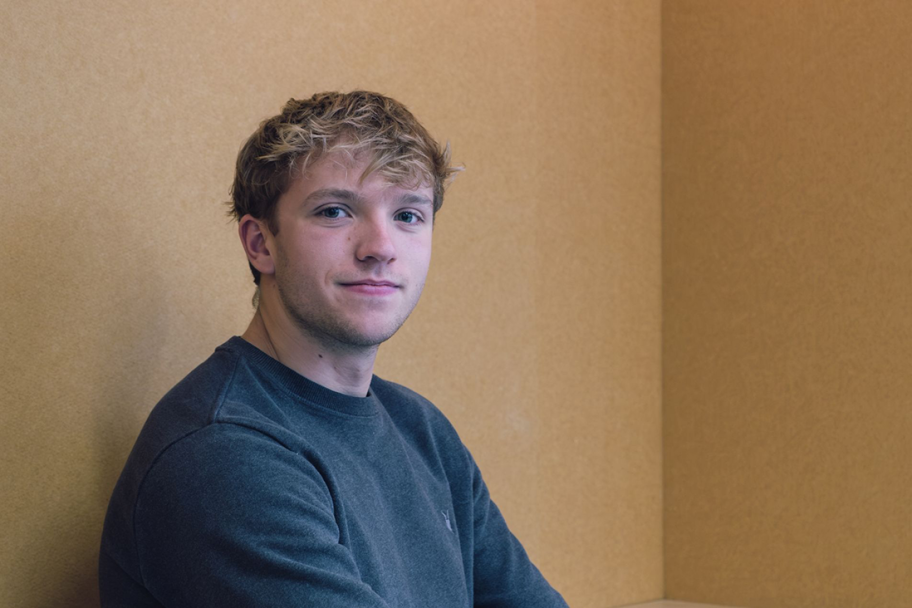 Tom Balsdon faces the camera smiling, he is wearing a grey jumper