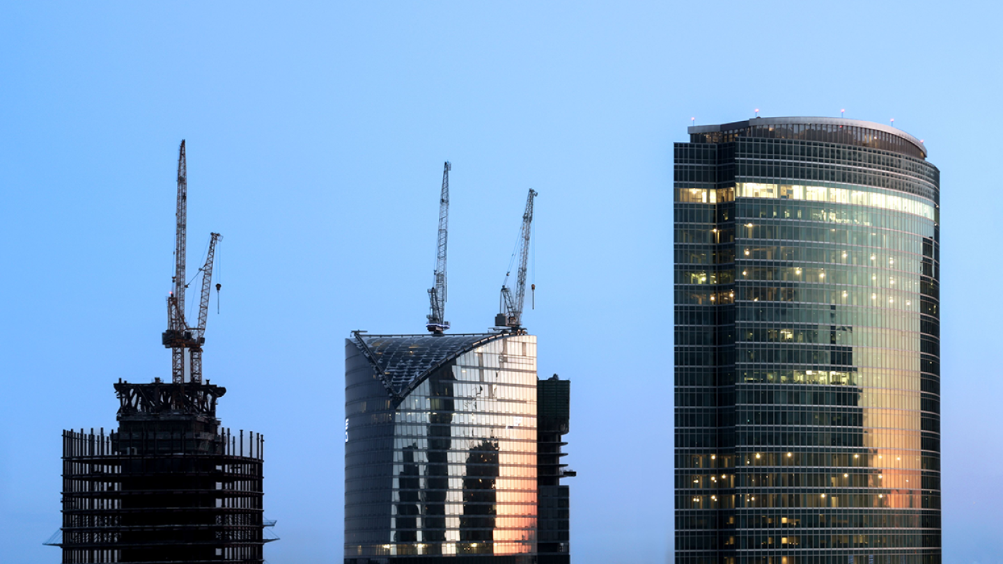 Tops of three towers of different heights, two of which have cranes coming off them