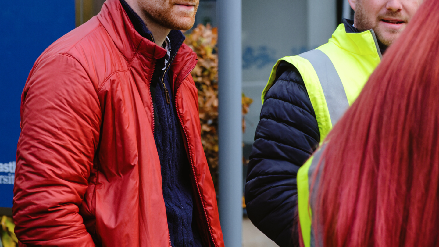 A man in a blue jumper and red jacket joins in conversation