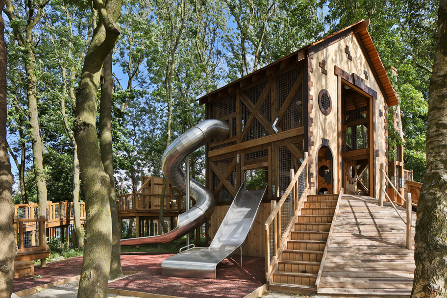 An image of a children's playground made from wood, with a metal slide curving around