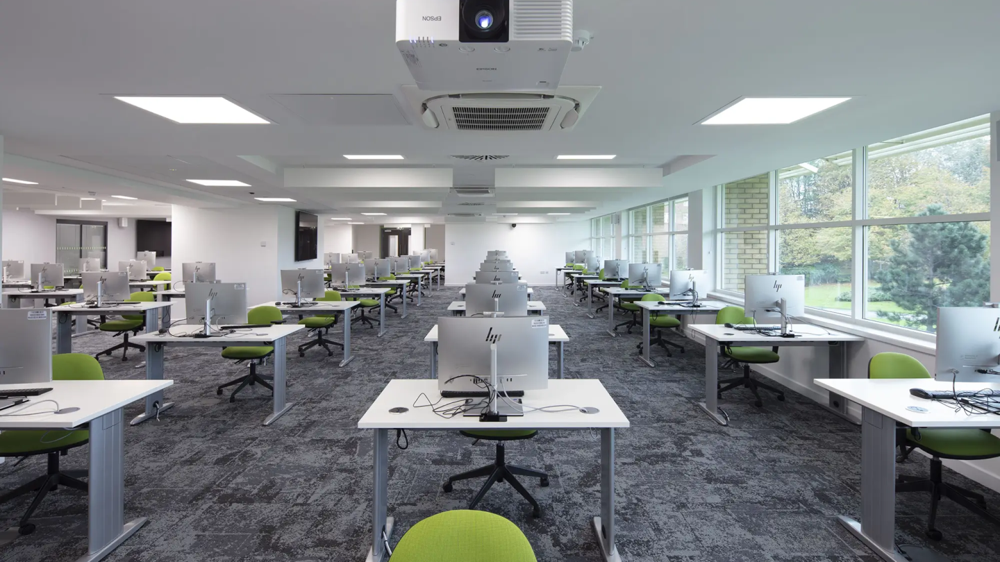 Rows of desks with silver HP desktops and lime green office chairs
