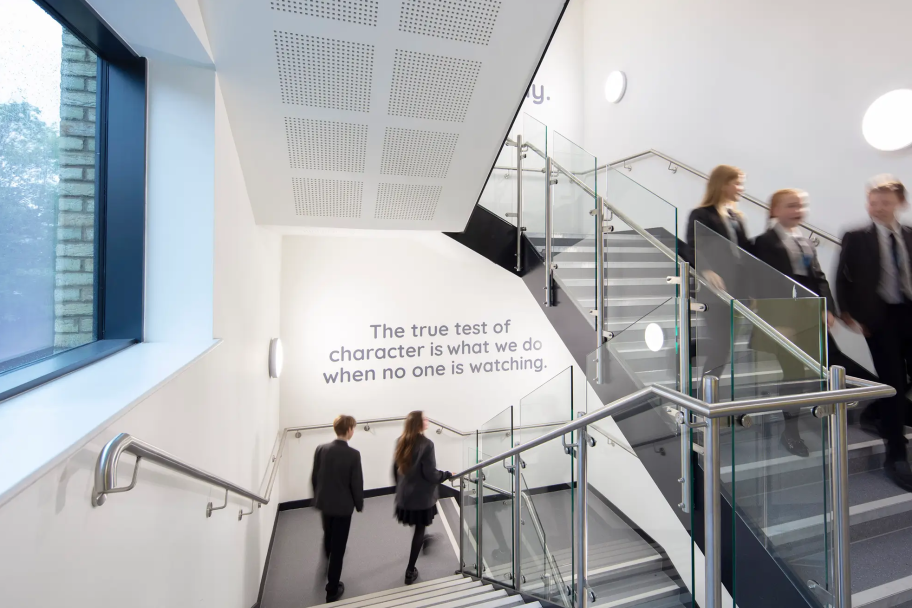Students walking down some stairs, there is an inspirational quote on the wall in front of them