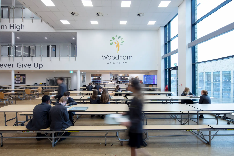 Woodham Academy dining halls, with large logo on the wall and several long benches for students to sit at
