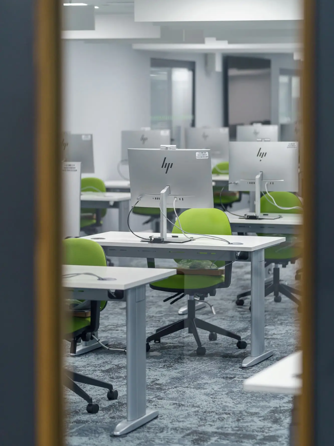 A through the window shot of the study spaces with a desk and lime green office chair