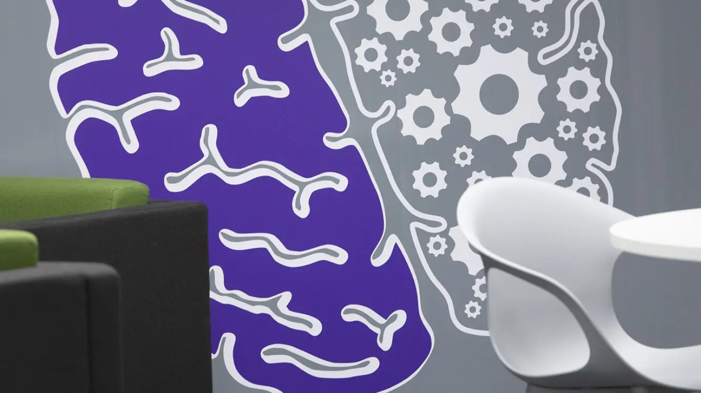 A close-up shot of the wall with a mural image of a brain- half of the brain is made from cogs and the other side is filled with purple