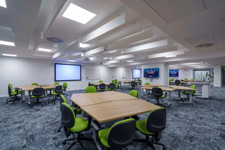 Collaborative study spaces with large tables and lime green office chairs and multiple large screens