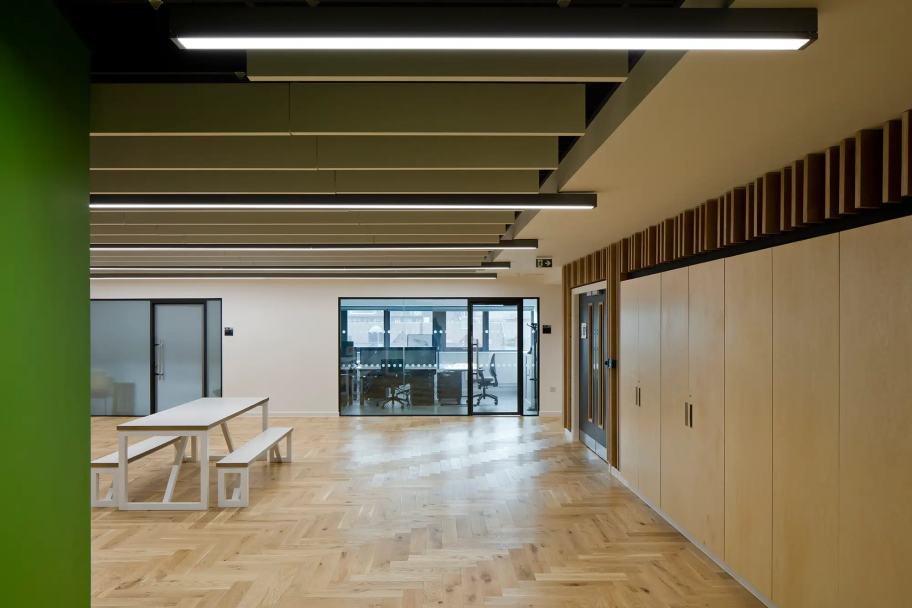 Inside a collaborative study space with a long white bench and acoustic ceiling panelling. There are several light wood and green accents.