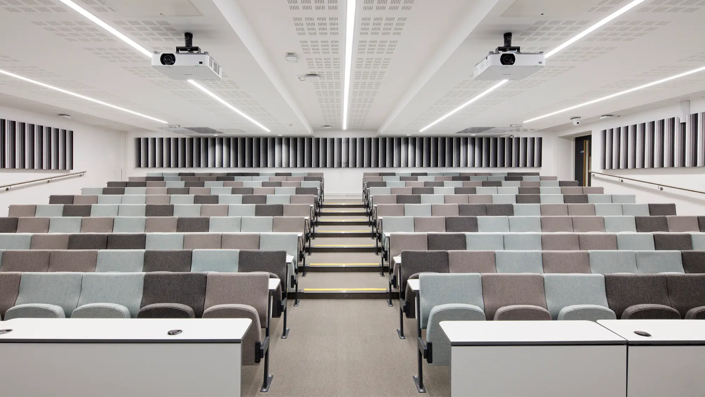 Inside a large lecture theatre with sound acoustic panelling on the walls and dark grey, light grey, and light blue seats