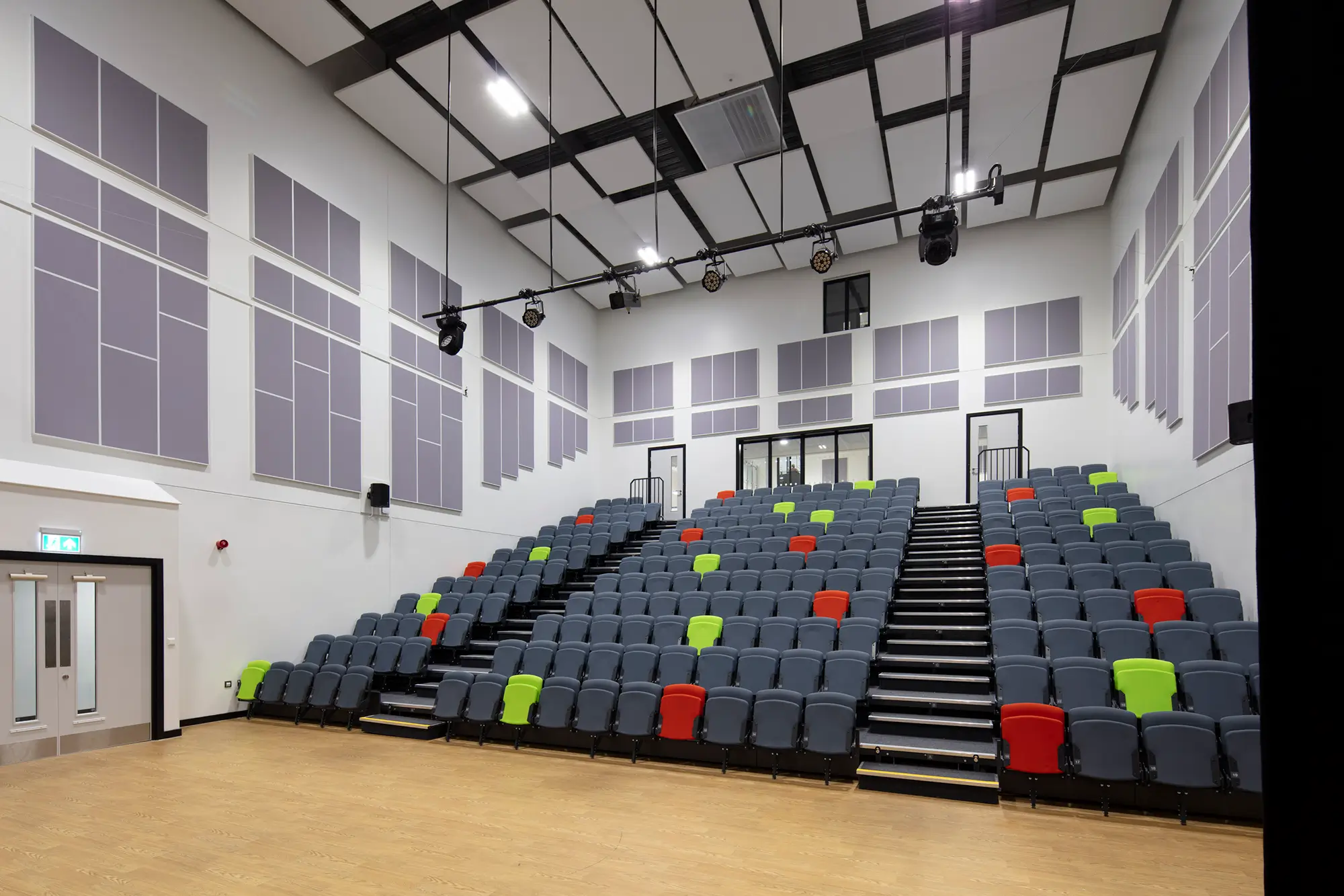 Woodham Academy theatre with several grey seats, sporadic green and red seats, and purple panelling on the walls