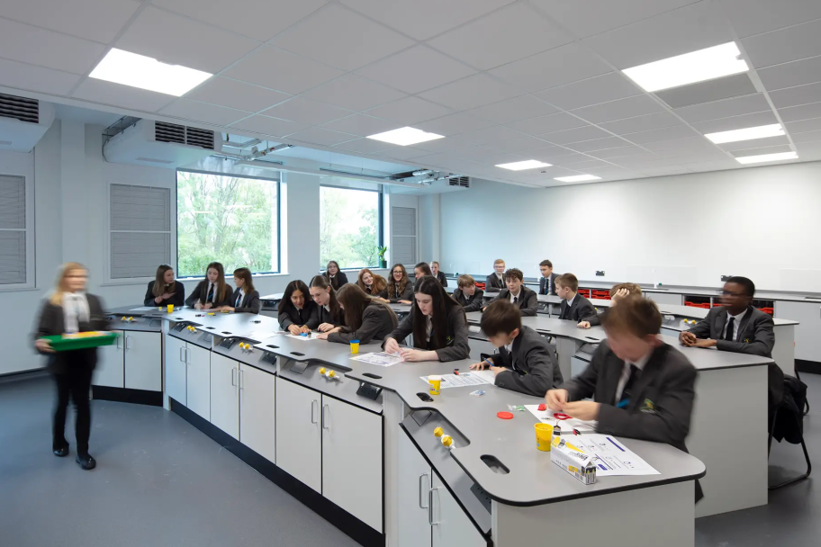 Inside a classroom, there are students wearing dark grey uniforms working at desks