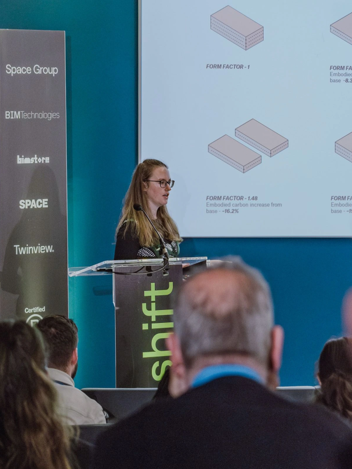 Catherine Sinclair portrait image, speaking at a podium with a presentation behind her showing building models